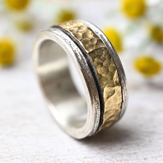 Meditationsring (Spinning Ring) aus Silber und 333 Gold, handgehämmertes Mittelband, vor weich fokussierten Kamillenblüten.